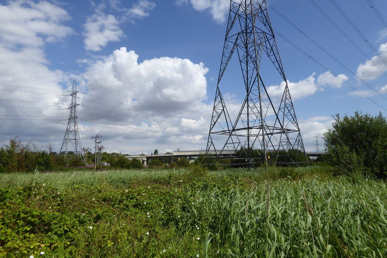 Electricity transmission pylons and power lines over reeds and scrub near Purfleet, Essex, under a blue sky with white clouds.